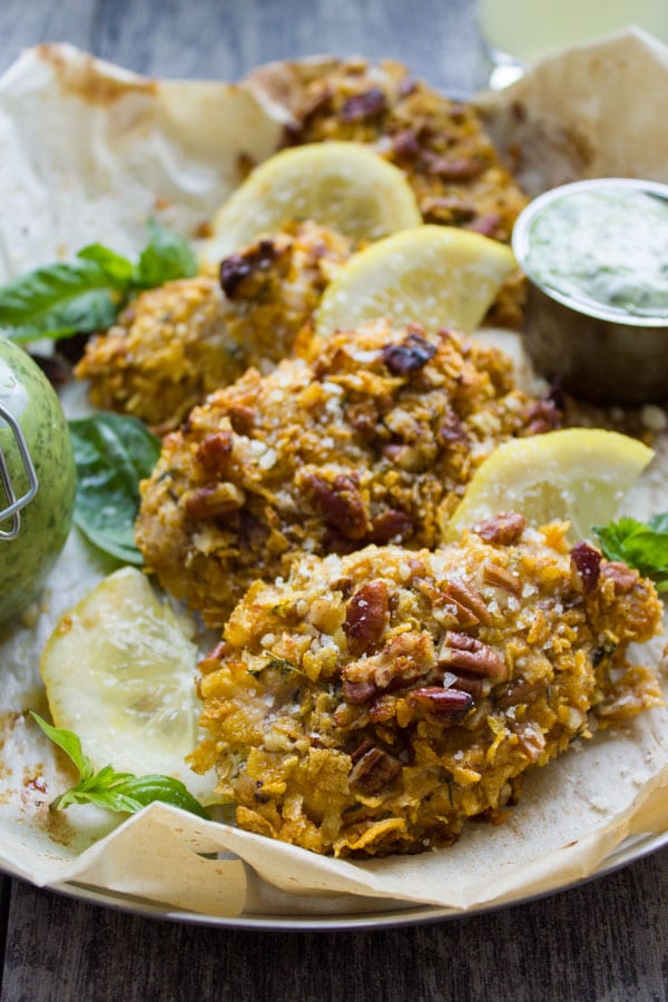 side view of Pecan Crust Baked Chicken Tenders served on parchment paper with a small bowl with basil dip on the side