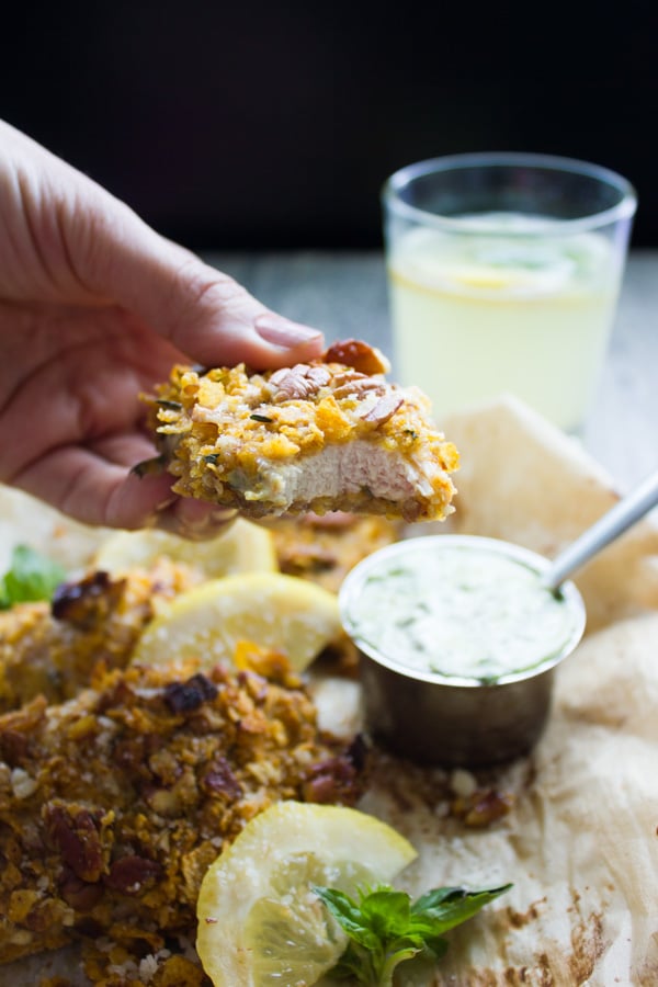 a hand holding a pecan crusted chicken tender with a bite taken out the front