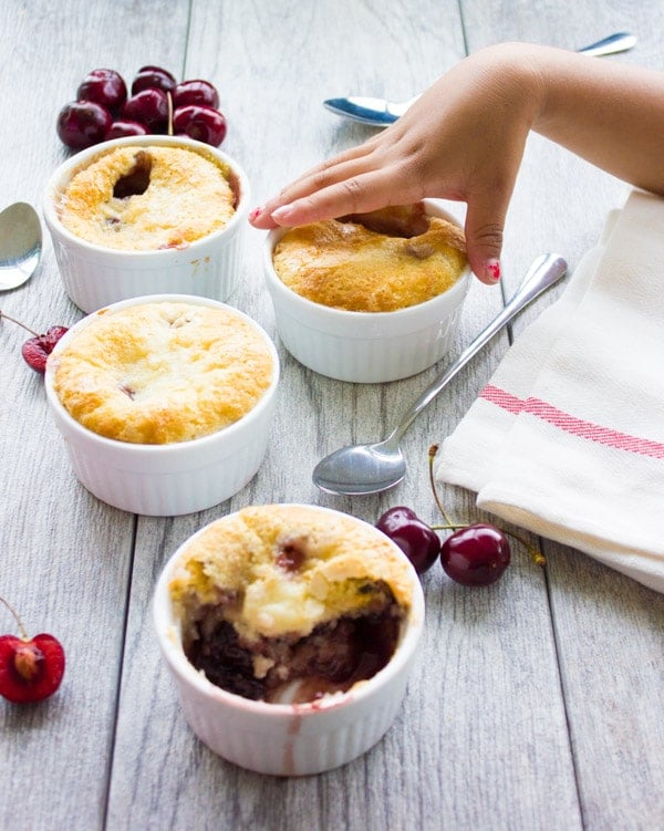 a child's hand reaching for a small ramekin of Sweet Cherry Buckle