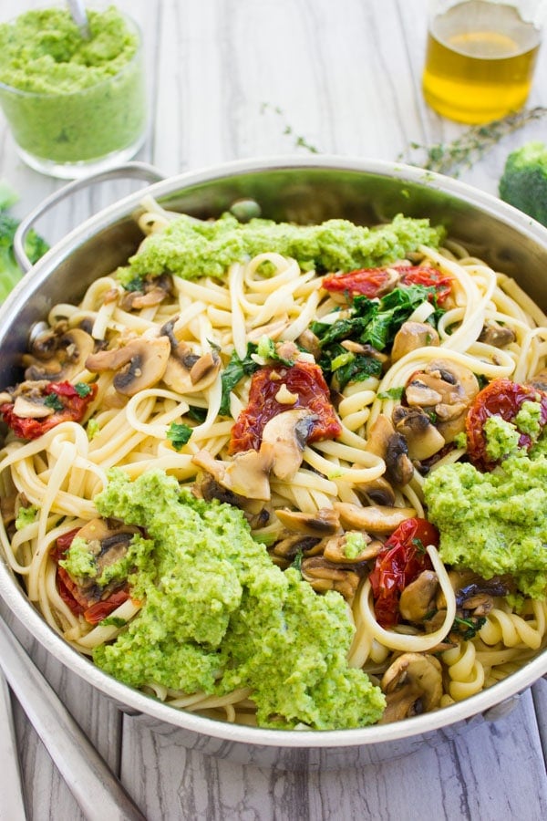 a skillet with pasta sauteed with mushrooms and tomatoes and topped with broccoli pesto