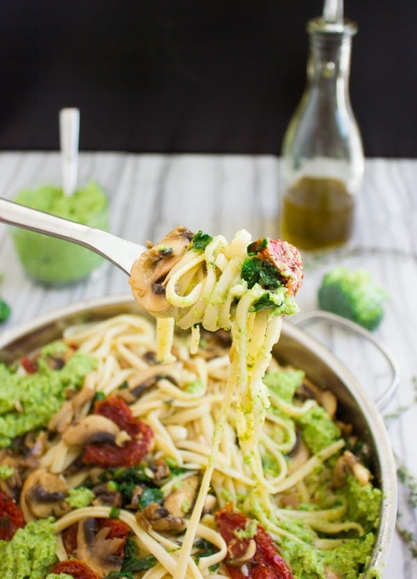 a fork full of broccoli pesto pasta with sun-dried tomatoes, mushrooms and olives