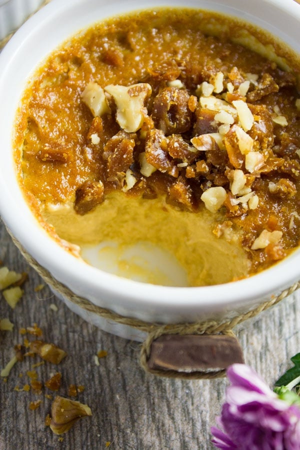 A close up of a ramekin with caramel pudding inside and half of it eaten off showing the creamy texture inside.