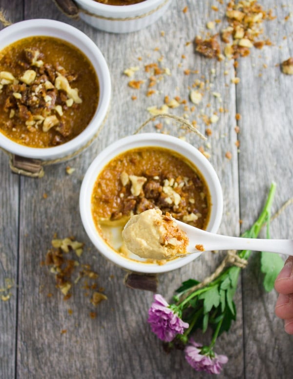 A spoon with a bite of homemade caramel pudding over a ramekin with the homemade caramel pudding