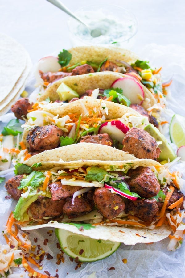 close-up of four tandoori chicken tacos filled with cilantro corn slaw with a small dish with yogurt dip in the background