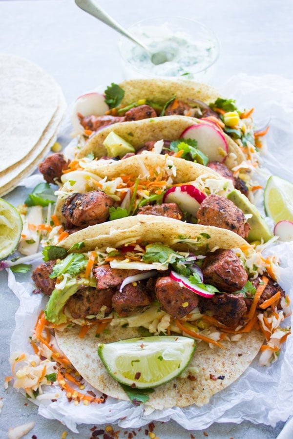 four tandoori chicken tacos with cilantro corn slaw lined up on parchment paper