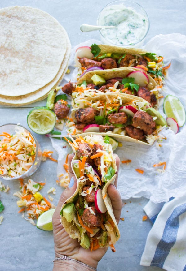 a hand holding a tandoori chicken taco with cilantro corn slaw