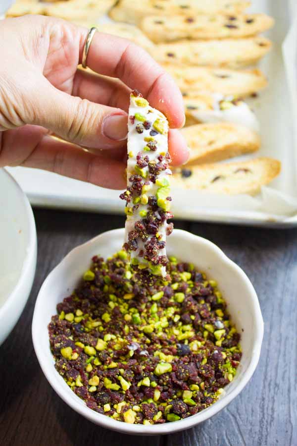 freshly glazed Cranberry Pistachio Biscotti being dipped into chopped pistachios and cranberries