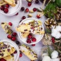 Two pieces of Cranberry Pistachio Biscotti on a plate surrounded by cranberries.