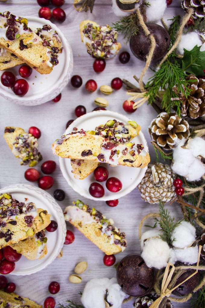 Two pieces of Cranberry Pistachio Biscotti on a plate surrounded by cranberries.