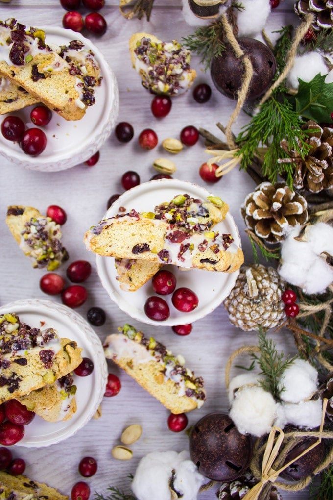 Two pieces of Cranberry Pistachio Biscotti on a plate surrounded by cranberries. 