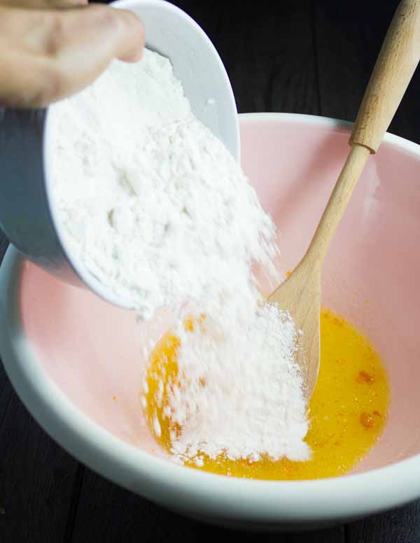 flour being added to a biscotti batter in a pink bowl