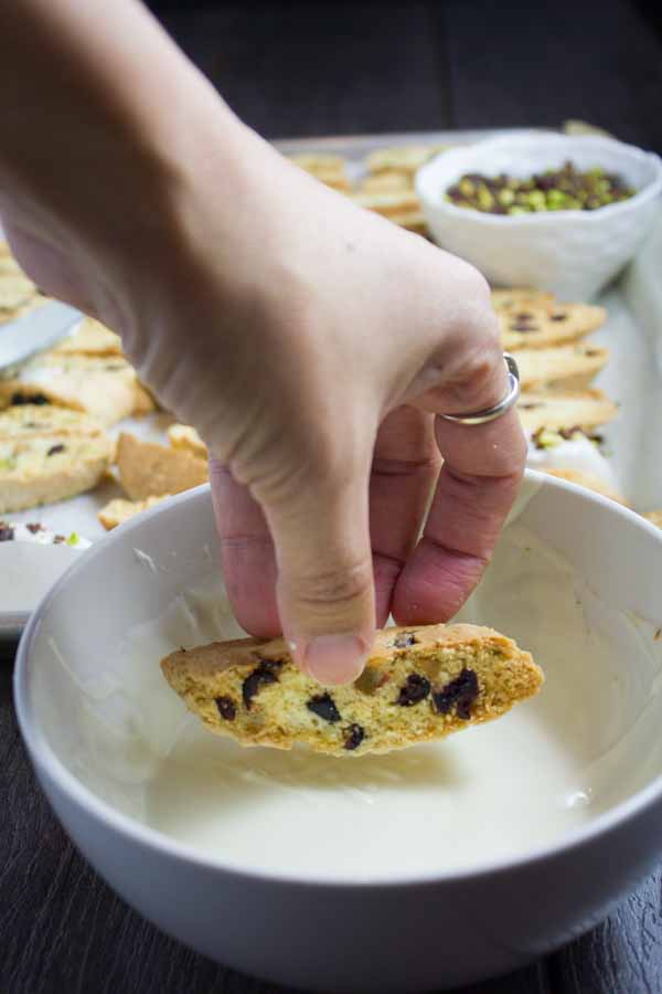 a Cranberry Pistachio biscotti being dipped into glaze