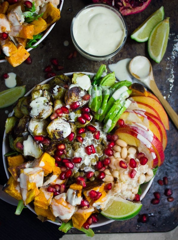 Lentil Fall Harvest Buddha Bowl topped with apples, roasted brussels sprouts, sweet potatoes and pomegranate arils with some tahini dressing on the side