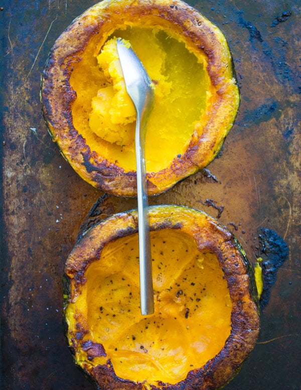the soft flesh being scooped out of a halved baked kabocha squash on a baking sheet