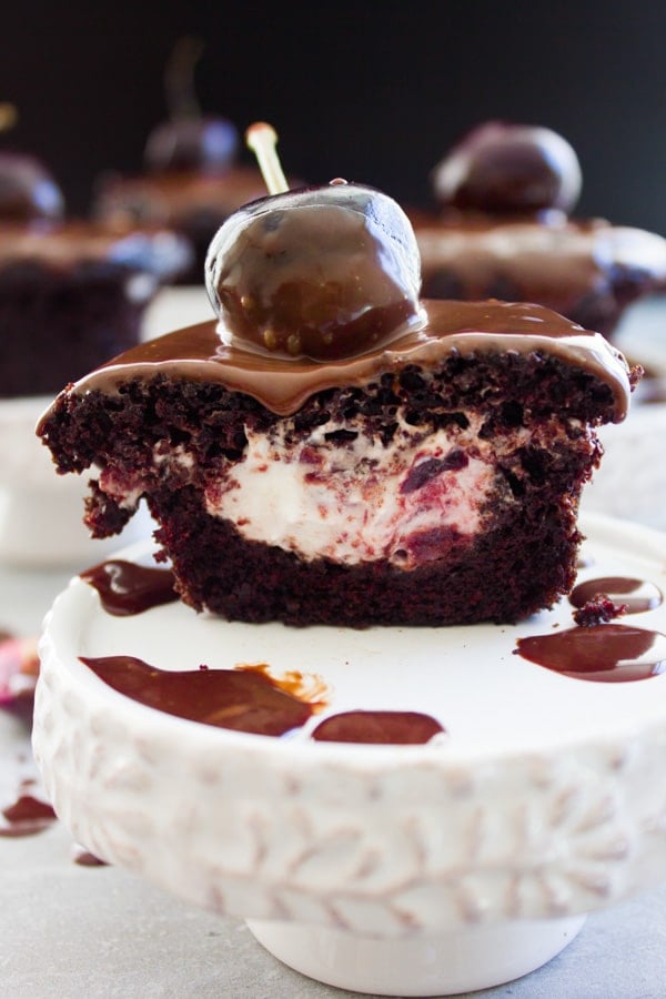a black forest cupcake cut in half to reveal the cherry studded whipped cream filling