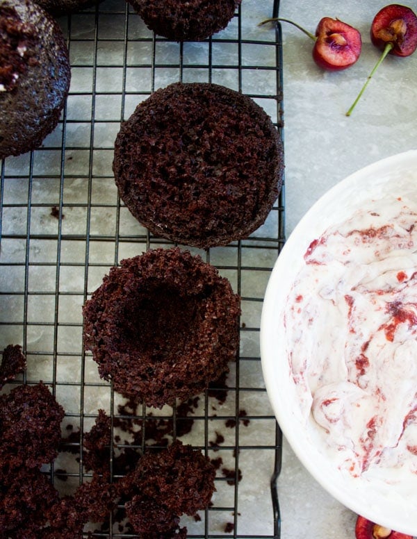 a hollowed out chocolate muffin next to a bowl of cherry whipped cream