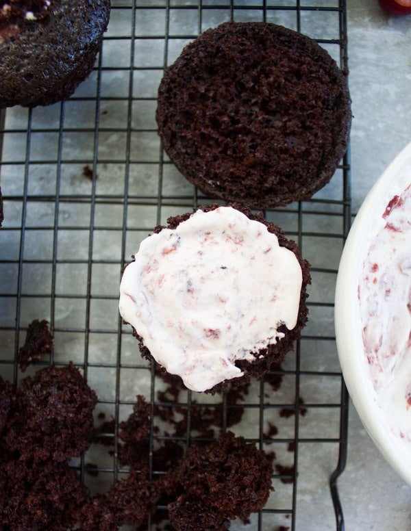 a chocolate muffin being filled with whipped cream and cherries to make black forest cupcakes