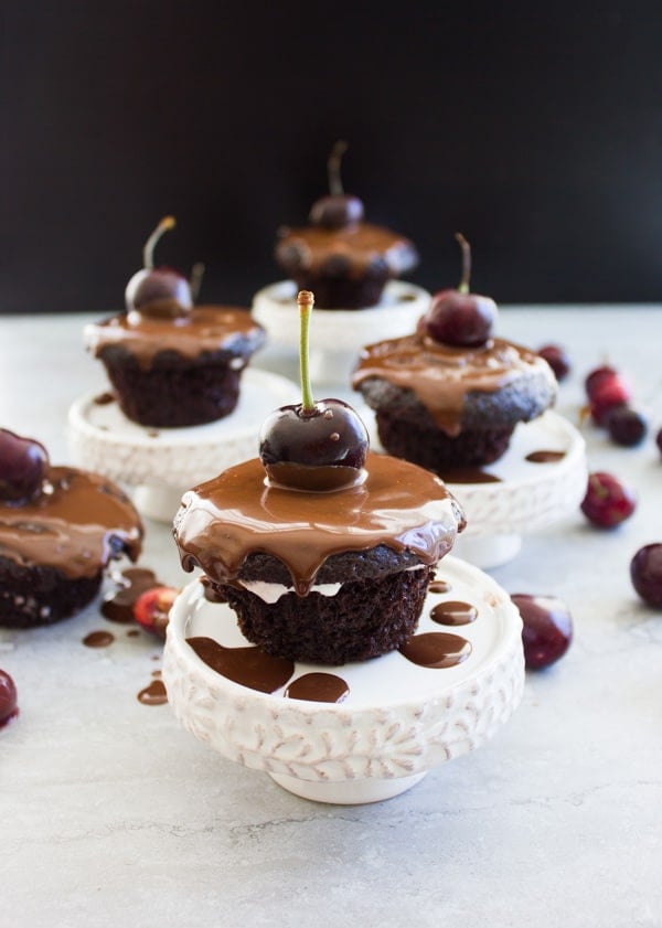 Easy Mini Black Forest Cupcakes drizzled with chocolate sauce on little white cupcake stands 