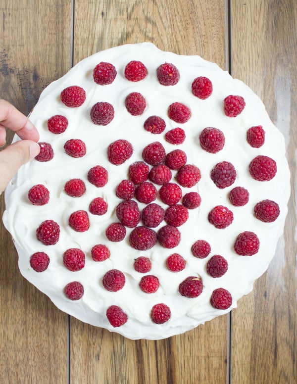 a vanilla cream cake being topped with fresh raspberries