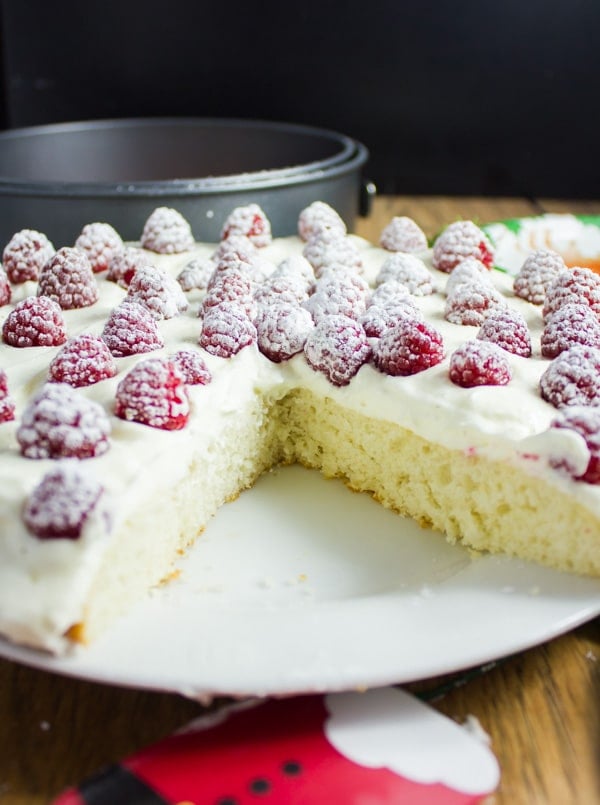 side view of a Fluffy White Raspberry Holiday Cake with a big piece cut out the front