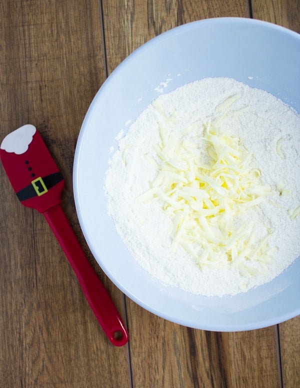 grated cold butter being added to dry ingredients in a bowl