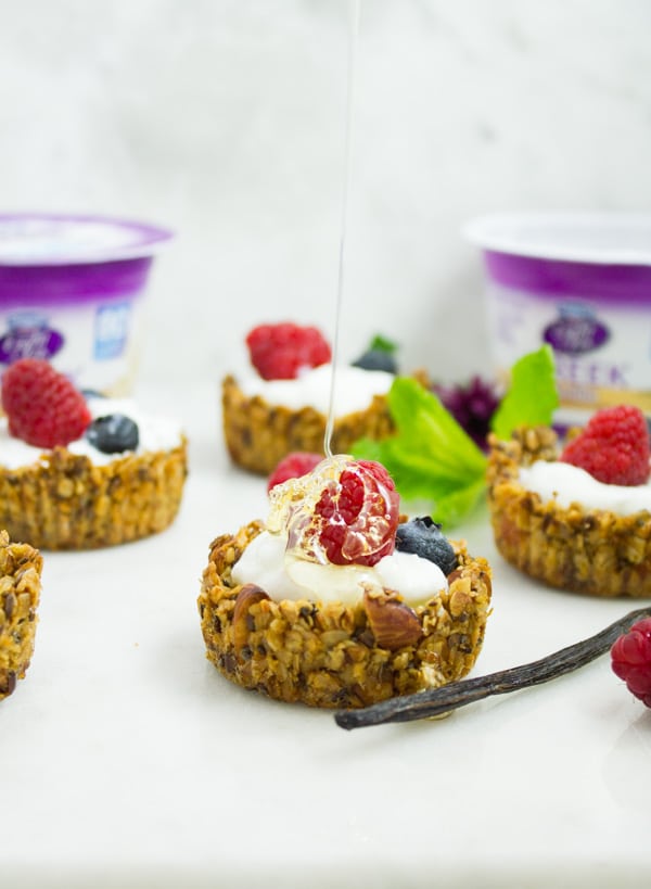 honey being drizzled on top of a Healthy Breakfast Granola cup filled with yogurt and berries