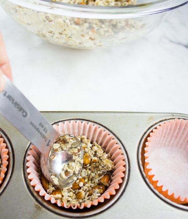 healthy granola being spooned into paper mold lined muffin tins