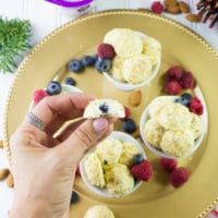 a hand holding an Almond Crunch Greek Yogurt Cheesecake Bite with a blueberry in the middle