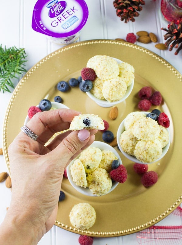 a hand holding an Almond Crunch Greek Yogurt Cheesecake Bite with a blueberry in the middle