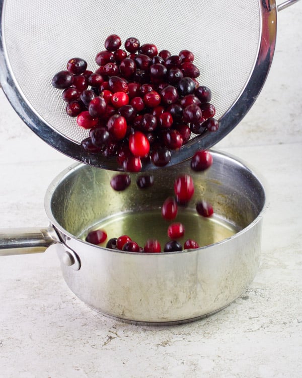 cranberries being added to orange simple syrup in a pot