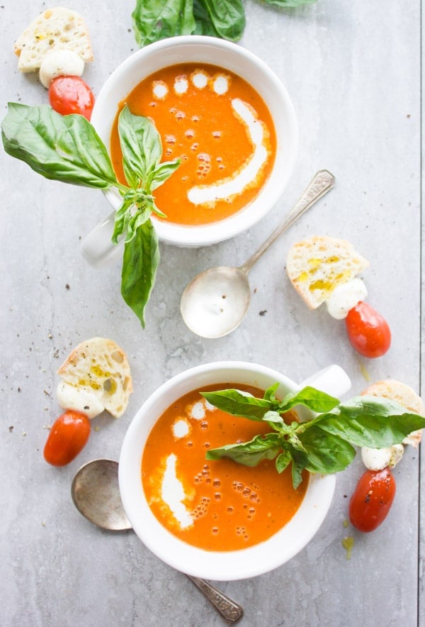 Two bowl of Carrot Tomato Basil Soup served with a drizzle of cream, fresh basil and some slices of white bread