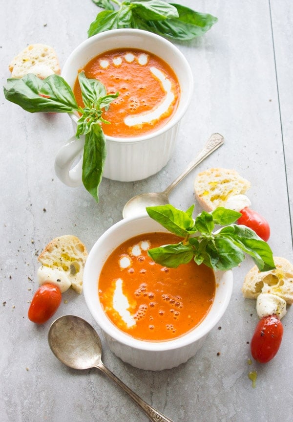 Two bowl of Carrot Tomato Basil Soup served with a drizzle of cream, fresh basil and some slices of white bread