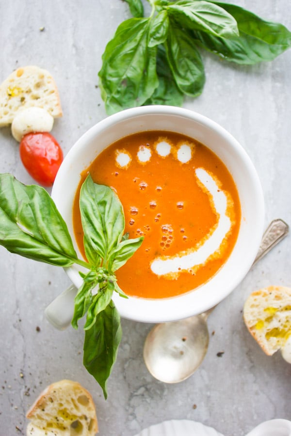 a bowl of Carrot Tomato Basil Soup served with a drizzle of cream, fresh basil and some slices of white bread