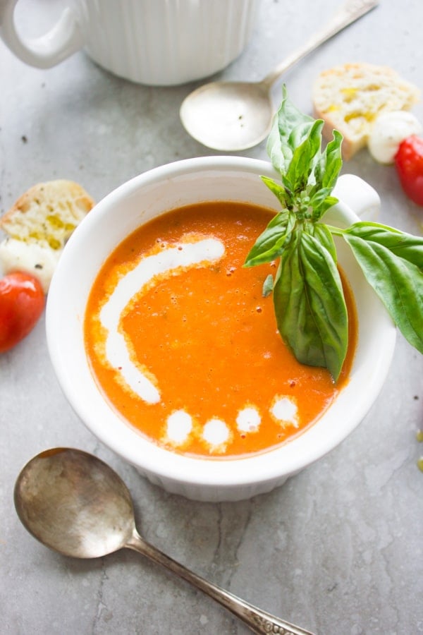 bowl of Carrot Tomato Basil Soup served with a drizzle of cream, fresh basil and some slices of white bread