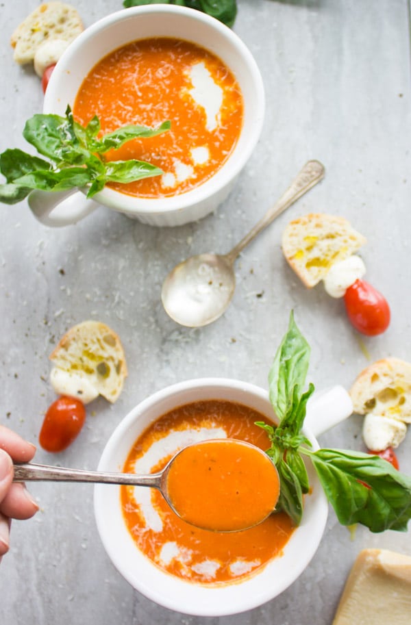 Two bowl of Carrot Tomato Basil Soup served with a drizzle of cream, fresh basil and some slices of white bread