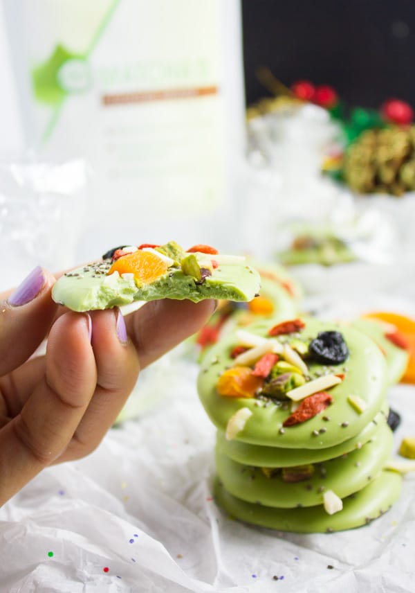 a hand holding half a piece of matcha green tea white chocolate bark topped with dried fruit