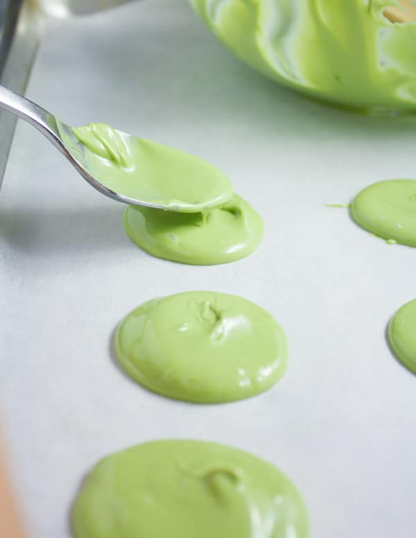 matcha infused white chocolate being spread onto parchment paper in little circles