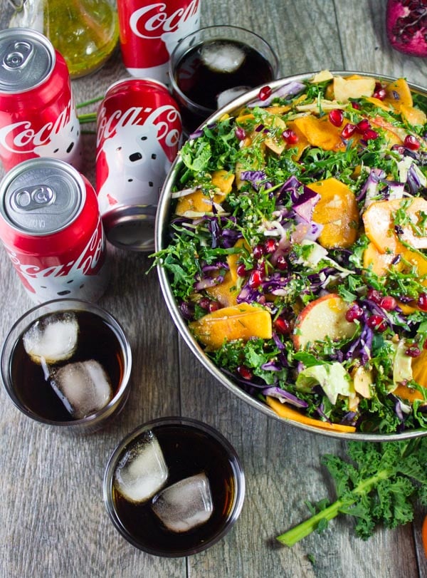 partial view of kale salad with apples, with some coke cans and filled glasses with coca-cola on the side