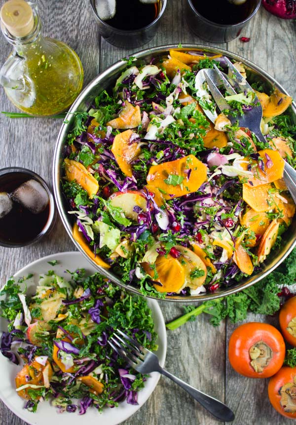 a small plate with kale salad in front of a big bowl with kale salad, apples, pomegranate seeds and persimmon slices