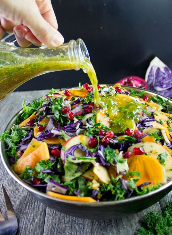 Coca-Cola Dressing being poured over a bowl with kale salad with apples, pomegranate seeds and shredded cabbage.