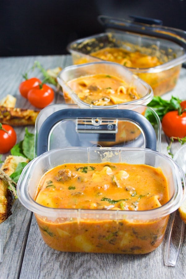 side view of a rubbermaid container with Lasagna Soup with tomatoes and breadsticks on the side