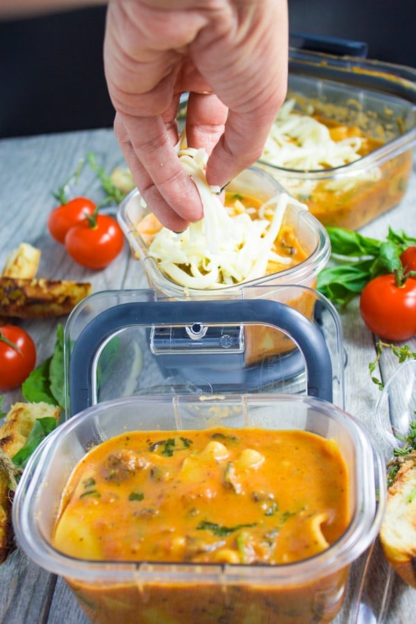 cheese being sprinkled on top of lasagna soup in a small plastic container