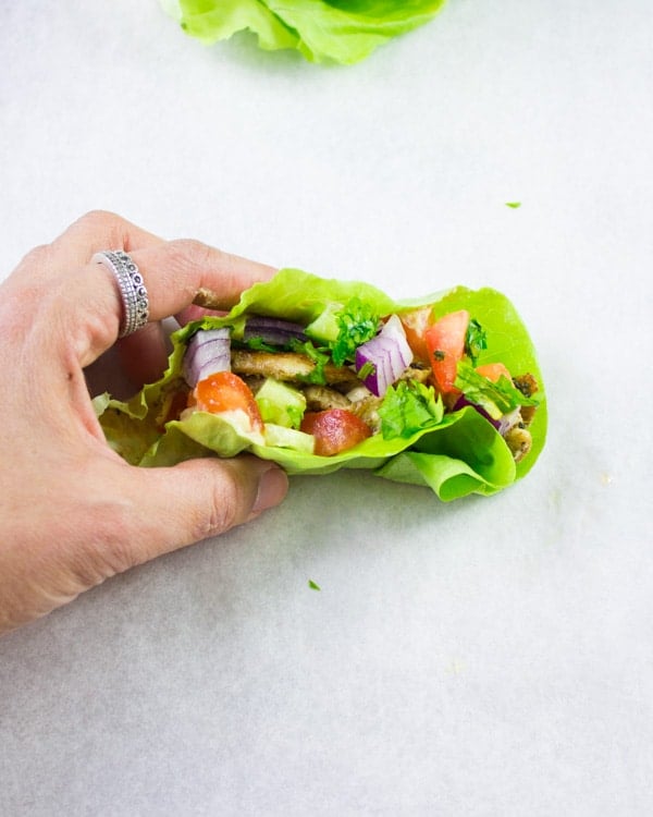 a hand holding a Chicken Shawarma Lettuce Cup against a white backdrop