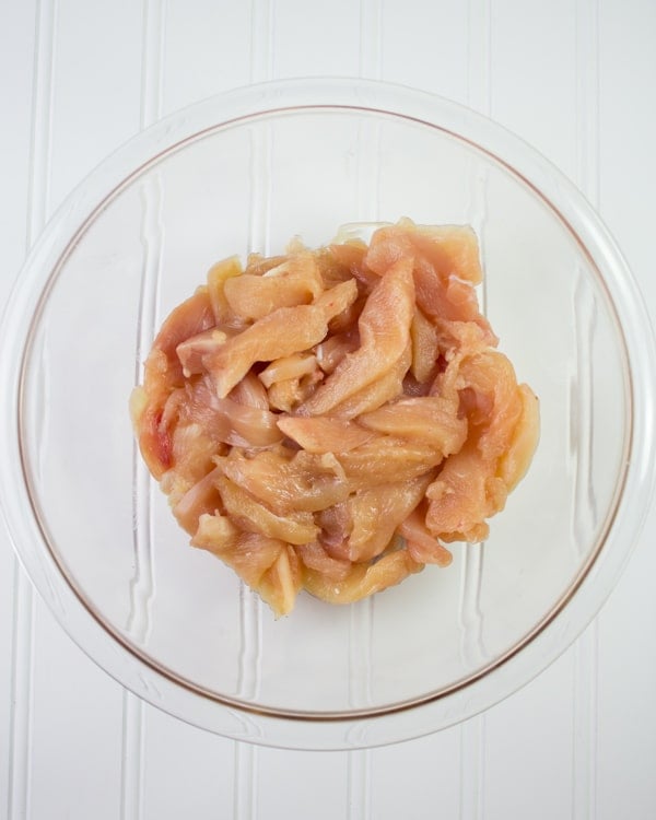 strips of skinless, boneless chicken in a glass bowl ready for seasoning