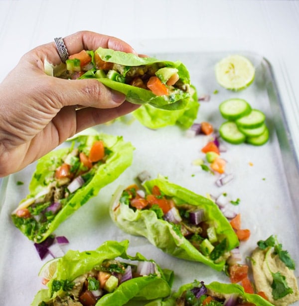 a hand holding a chicken shawarma lettuce cup against the backdrop of a sheet pan with more lettuce cups