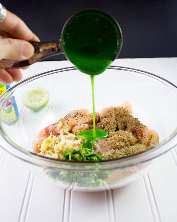 green habanero chili sauce being added to a bowl with seasoned uncooked chicken strips