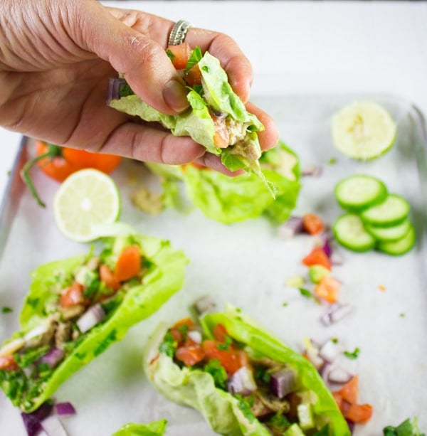 a hand holding a chicken shawarma lettuce cup against the backdrop of a sheet pan with lettuce cups