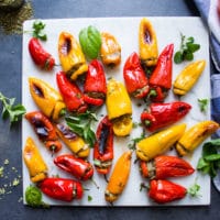 A marble with lots of stuffed peppers surrounded by fresh herbs