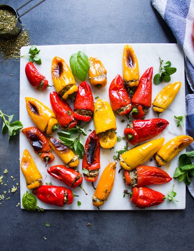 A marble with lots of stuffed peppers surrounded by fresh herbs