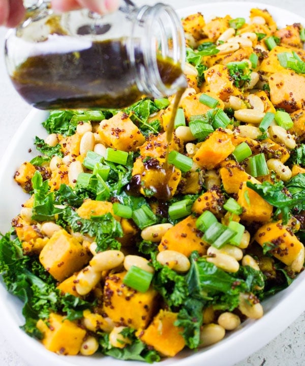 balsamic dressing being poured on top of One Pot Quinoa Sweet Potato Salad served in an oval salad bowl sprinkled with slivered almonds and chopped scallions